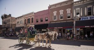 Two people driving a horse drawn uncovered wagon down Main Street in Deadwood, SD.