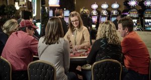 People sitting around a live gambling table with dealer seated behind it.