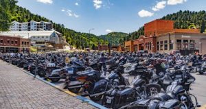 Many motorcycles fill an entire parking lot in Deadwood, SD. In the distance there is the Silverado, the Deadwood Mountain Grand, and the Black Hills National Forest.