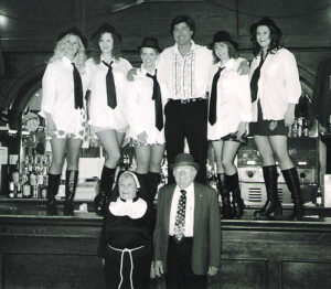 Deadwood Singing Nuns - A black and white picture from the original act showing five women in black skirts, white button up shirts, black ties. They are standing on top the bar at the Saloon 10 with two men and an additional women dressed as a nun. 