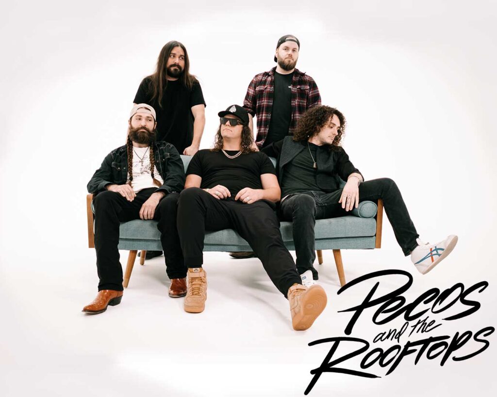 photo of five men on a white background. Three are sitting on a light teal couch and two are standing behind the first three.