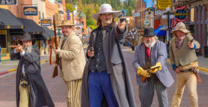Five men in period costume reenacting a historic shootout on Deadwood's Main Street.