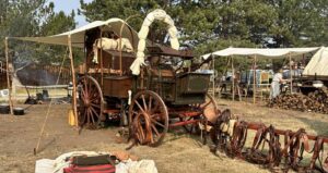 Deadwood's Chuckwagon Gathering and Cowboy Show with a picture of one of the historic and authentic wooden chuckwagons. the Wagon has a green body, red wheels and a canvas cover that is rolled up along the top.